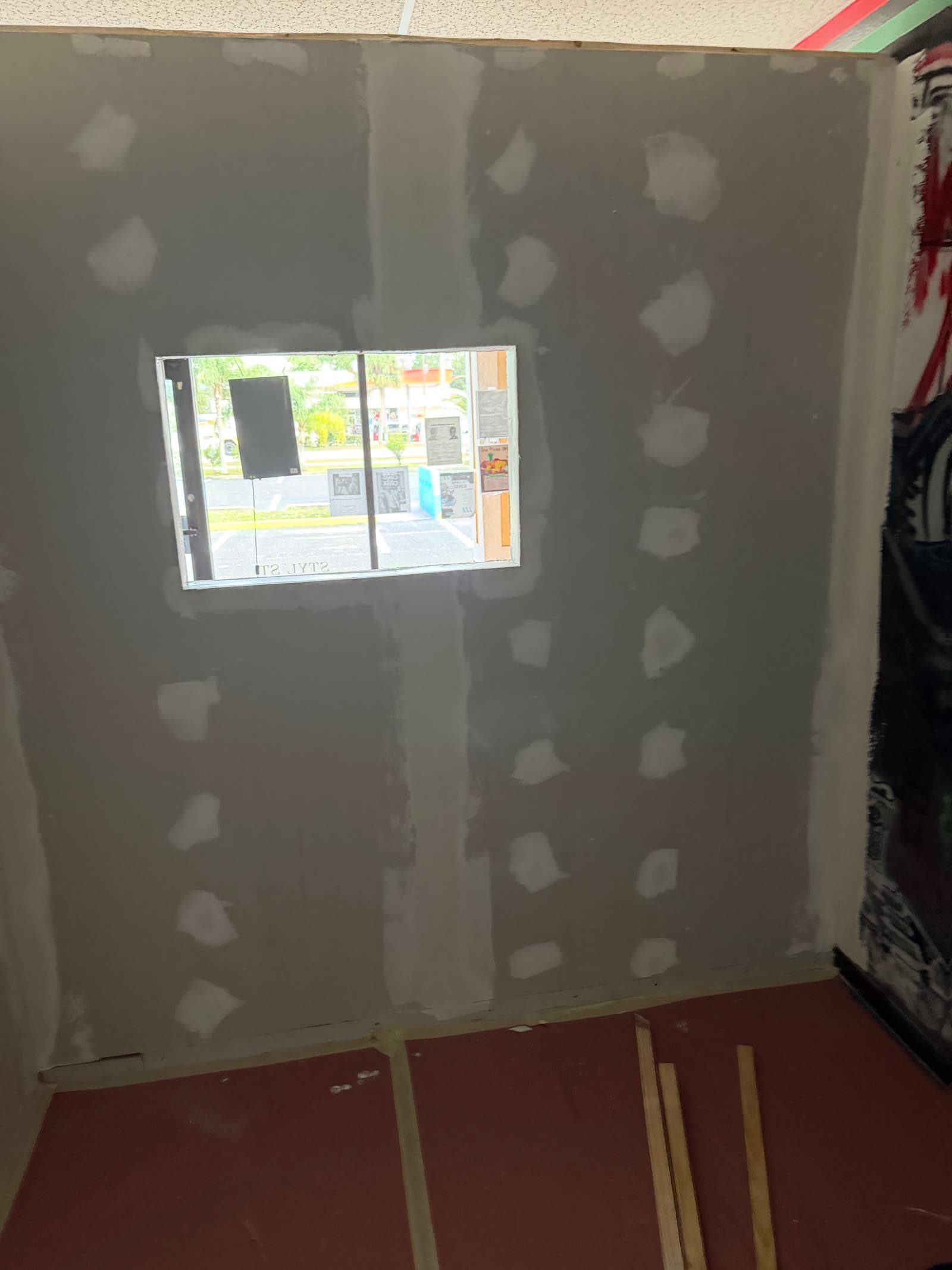 Interior viewing window surrounded by newly finished drywall at Exodus Barbershop